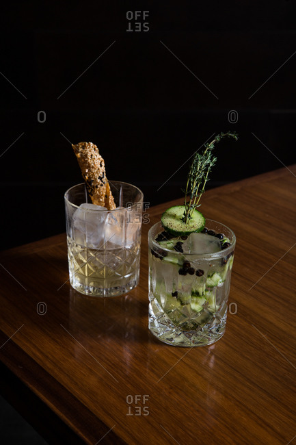 Two cocktails with edible garnishes served on a wooden table with black background