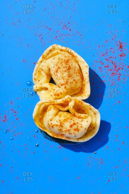 Two cooked tortellini sprinkled with paprika on a blue background