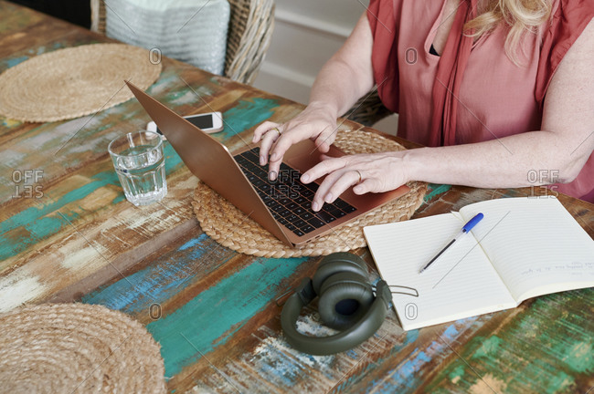 Closeup of a mature woman working online with a laptop and writing notes while working alone at a table in her apartment