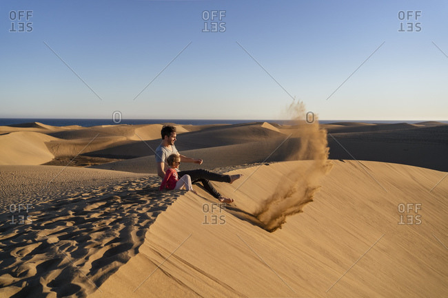 Father and daughter sitting on sand dune- Gran Canaria- Spain