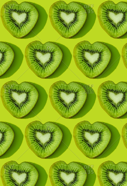 Heart shaped kiwi fruit slices pattern on green background