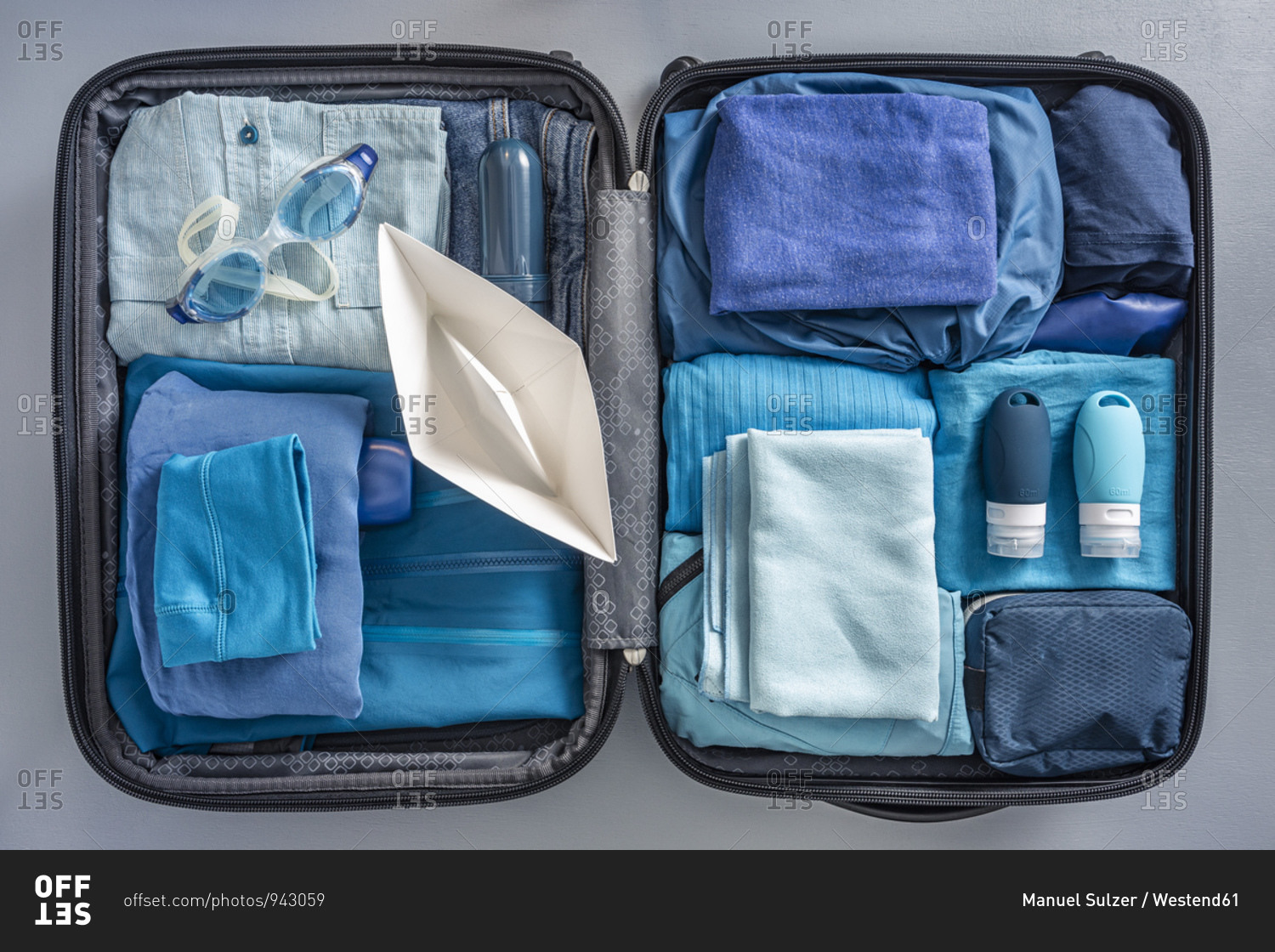 Overhead view of packed suitcase with clothes- swimming goggles and paper boat