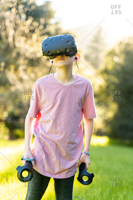 Boy standing with VR technology on while outdoors on sunny day