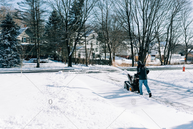 Young man snowplowing his driveway after a winter storm.