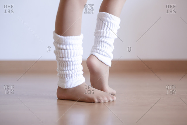 Closeup of unrecognizable girl putting on leg white warmers during ballet practice in studio, copy space