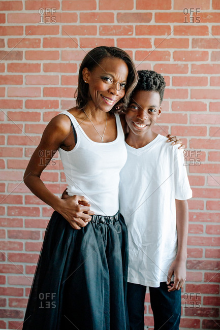 Smiling African American mother & son standing in front of brick wall