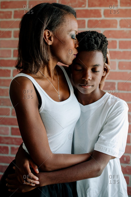 Loving African American mother with closed eyes embraces preteen son