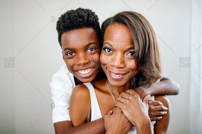 Handsome happy preteen black boy hugging beautiful mom from behind