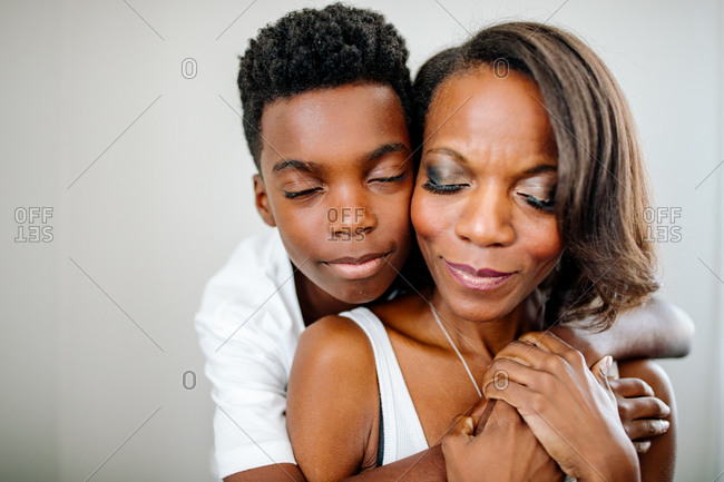 Tender embrace between Black mom & preteen son with eyes closed
