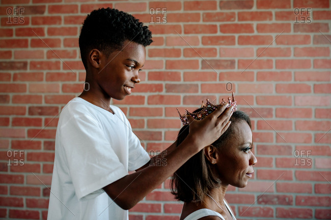 Smiling Black boy puts crown on pretty seated mom
