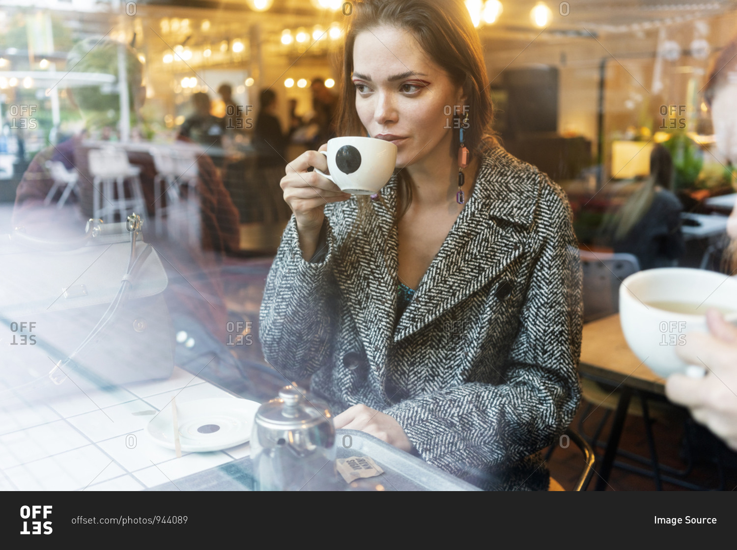 Young woman drinking coffee with friend in cafe, London, UK