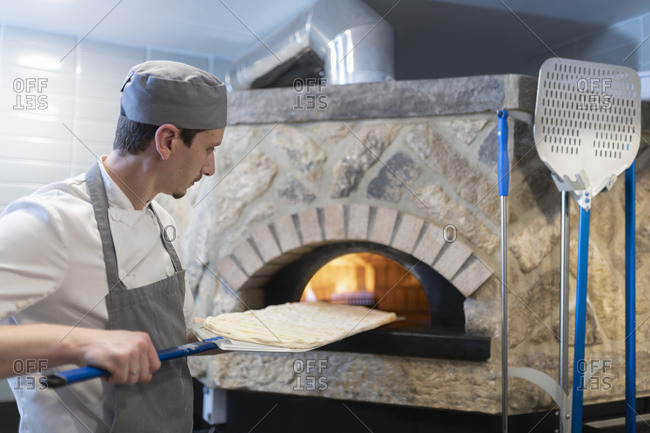 Chef putting dough of Pinsa Romana, a Roman style pizza blend reducing sugar and saturated fat, containing rice and soy with less gluten, into the oven