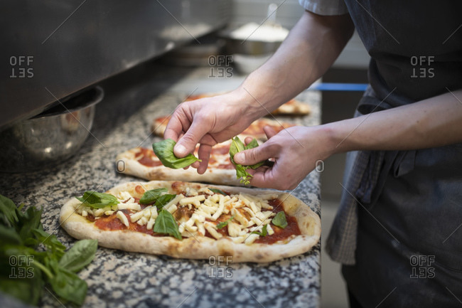 Chef placing basil onto Pinsa Romana base, a Roman style pizza blend reducing sugar and saturated fat, containing rice and soy with less gluten, close up of hands