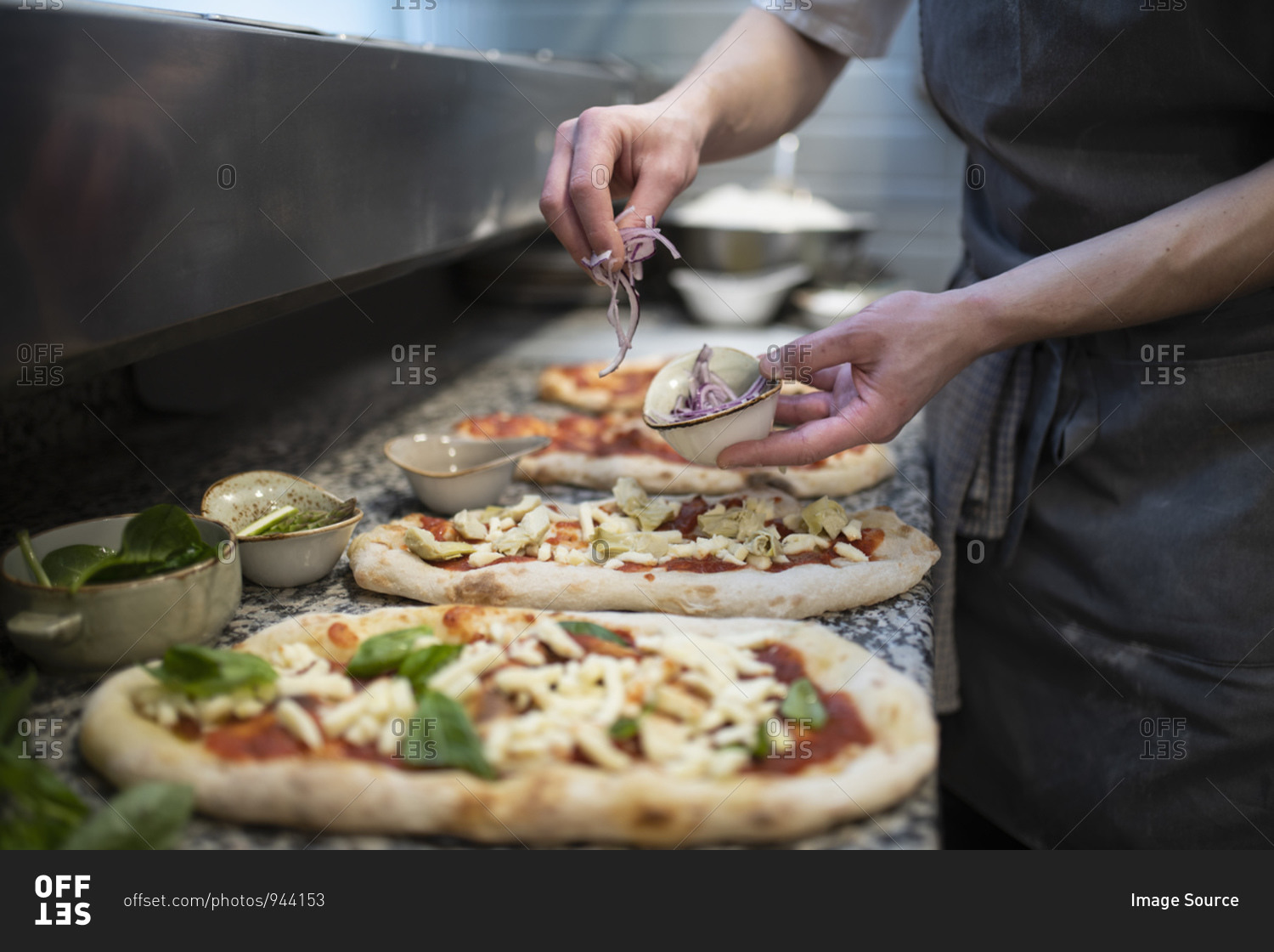 Chef placing onions onto Pinsa Romana base, a Roman style pizza blend reducing sugar and saturated fat, containing rice and soy with less gluten, close up of hands