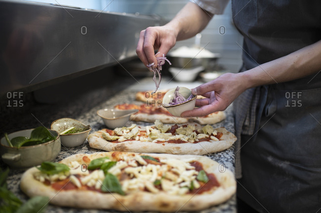 Chef placing onions onto Pinsa Romana base, a Roman style pizza blend reducing sugar and saturated fat, containing rice and soy with less gluten, close up of hands
