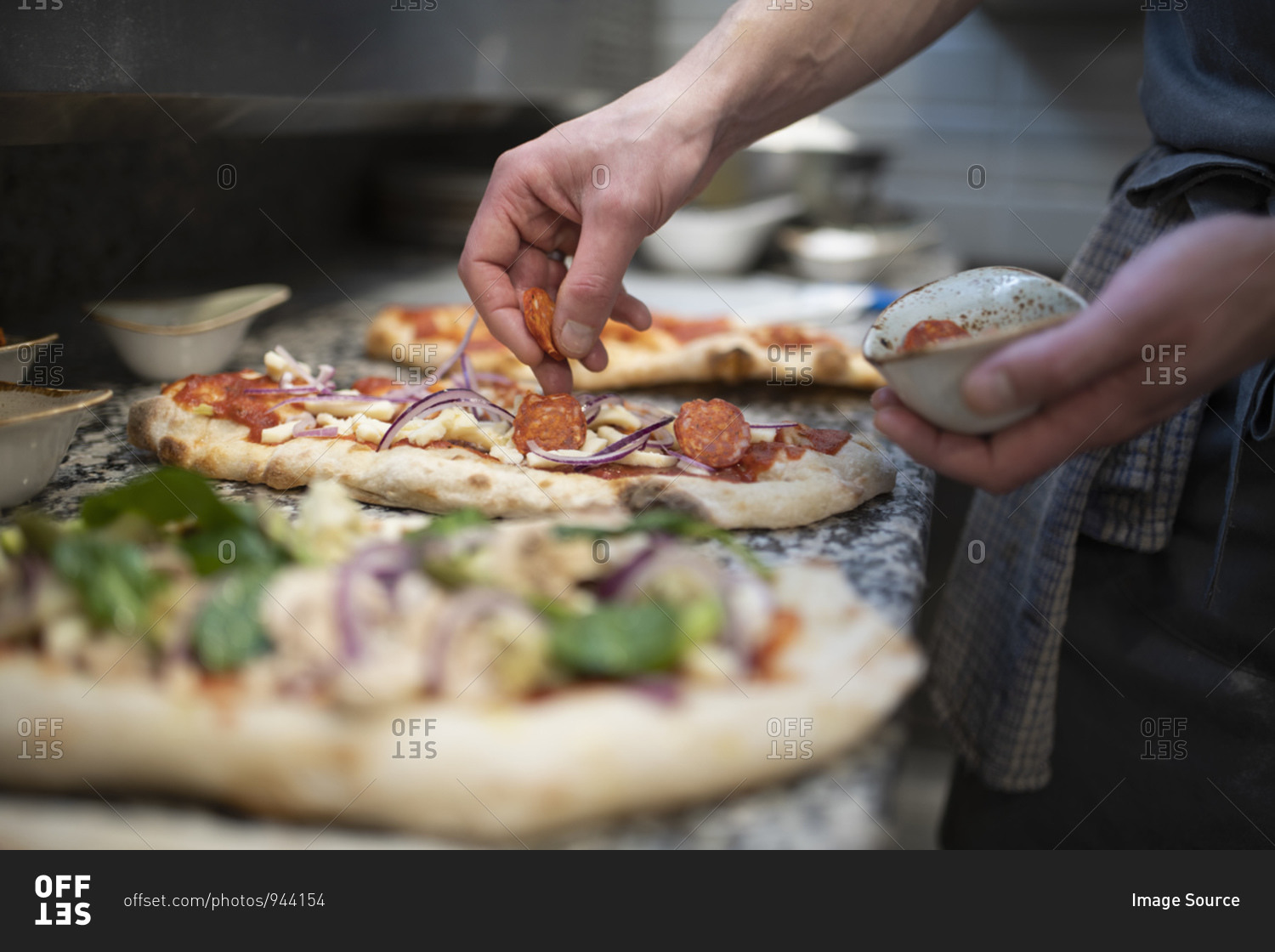 Chef placing sausage onto Pinsa Romana base, a Roman style pizza blend reducing sugar and saturated fat, containing rice and soy with less gluten, close up of hands