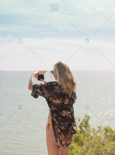 Woman taking photograph of sea on sunny day
