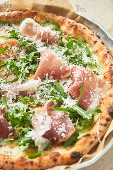 Pizza with arugula and prosciutto on marble surface