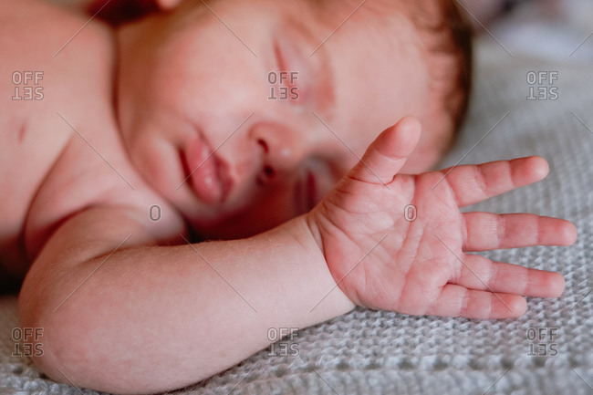 Calm cute infant with closed eyes covered with blanket resting in bed against blurred interior of light bedroom