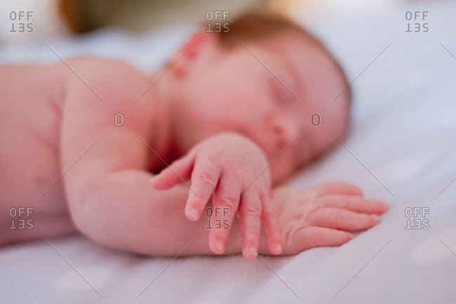 Calm cute infant with closed eyes covered with blanket resting in bed against blurred interior of light bedroom