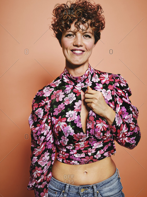 Fashionable happy pretty female model in stylish colorful crop top with floral print standing against pink background looking at camera
