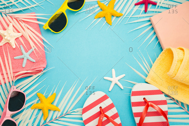 Top view composition of sunglasses and flip flops placed with beach towel and notebook on blue background with palm leaves and starfish representing summer vacation on beach