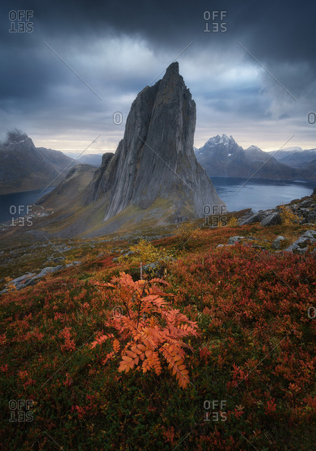 Segla mountain located in grassy valley near calm basin against dark overcast sky on island of Senja, Norway