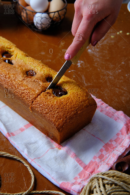 From above anonymous woman using knife to cut yummy sponge chocolate cake on towel on table in kitchen
