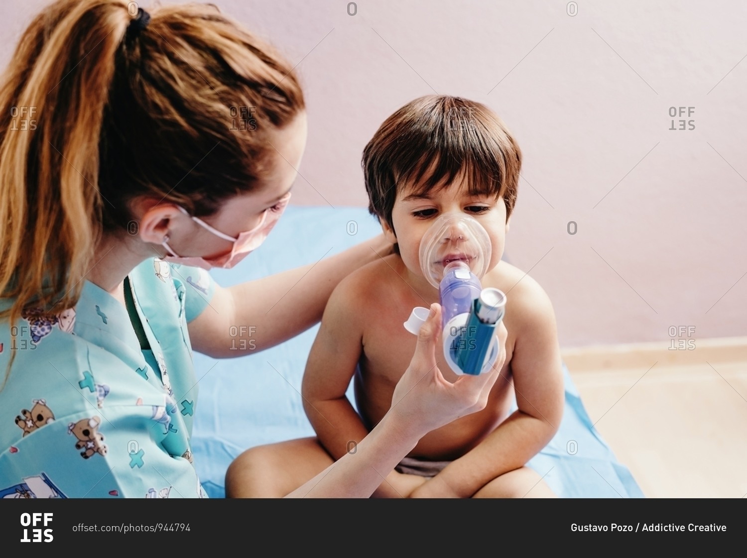 Side view of young female pediatric doctor in medical mask doing inhalation treatment with nebulizer for little boy having respiratory problem in hospital