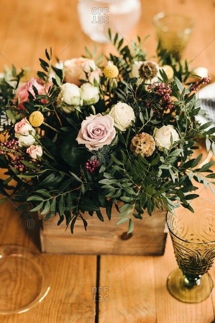 From above bouquet of miscellaneous flowers and green plant twigs in a wooden box on a timber table set for a meal