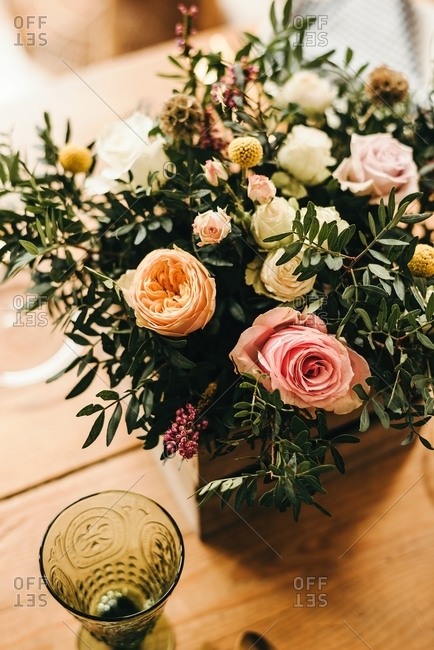 From above bouquet of miscellaneous flowers and green plant twigs in a wooden box on a timber table set for a meal