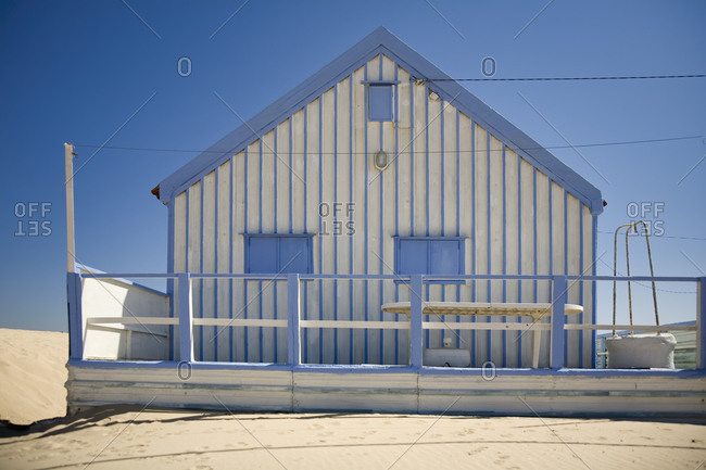 Small white and blue strips country house with white fence located at seaside against cloudless blue sky in sunny day