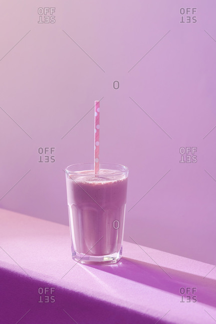 High angle of healthy delicious dairy beverage with fresh berries in transparent glass with straw on table in vivid purple light