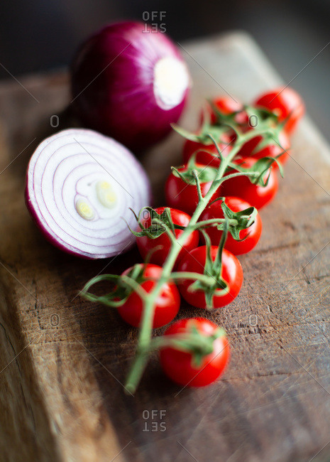 Bunch of fresh ripe tomatoes cherry and cut red onion bulbs placed on wooden cutting board