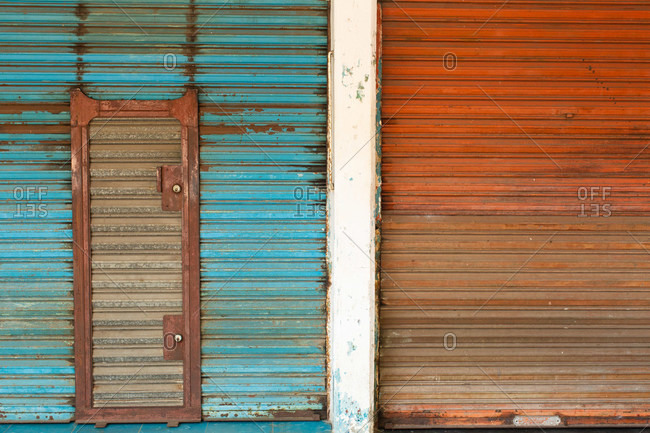 Weathered rusty metal shutter doors painted in blue and red color with shut doorway