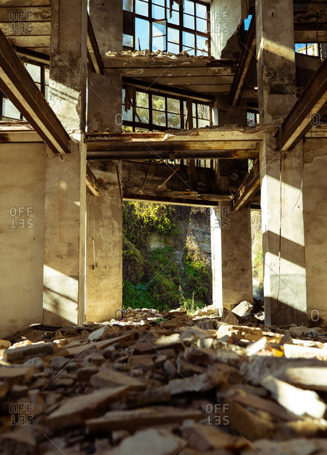 Low angle inside of aged abandoned disrupted city building with trash on floor lightened by sun rays