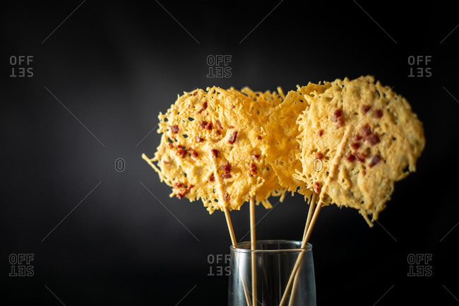 Glass with rice for decoration of crispy grated cheese chips on sticks placed on black background