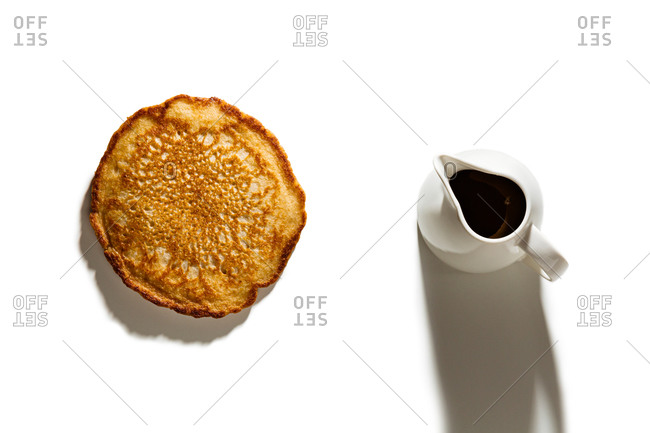 Pancake with pitcher of syrup on white background