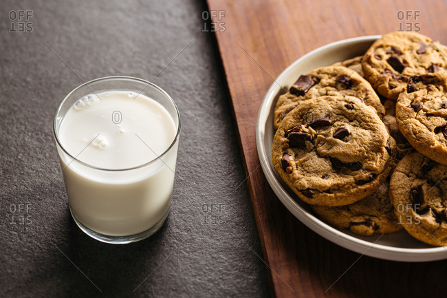Glass of milk and plate of chocolate chip cookies on cutting board