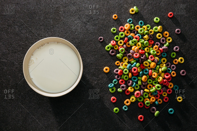 Bowl of milk next to pile of colorful cereal on table