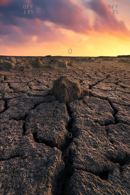 From above of drought cracked lifeless ground under colorful cloudy sky at sunset time