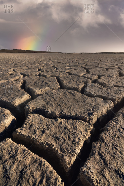 From above of drought cracked lifeless ground under colorful cloudy sky at sunset time