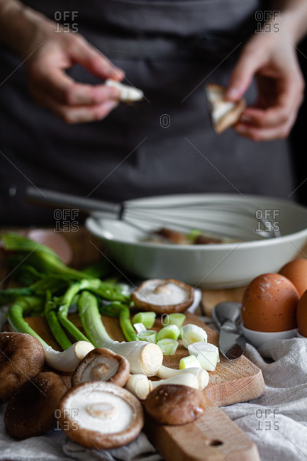 Bunch of fresh scallions and mushrooms placed on cutting board near eggs and poppy seeds against crop housewife mixing ingredients in bowl