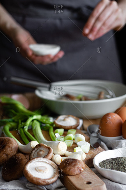 Bunch of fresh scallions and mushrooms placed on cutting board near eggs and poppy seeds against crop housewife mixing ingredients in bowl