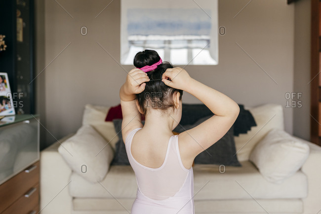 Back view of anonymous cute little dancer in leotard doing hair bun before ballet training in cozy living room at home