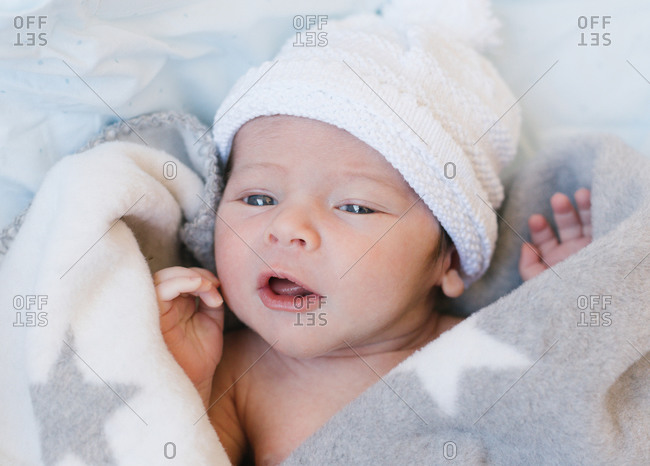 Cute baby in blanket and hat lying on bed