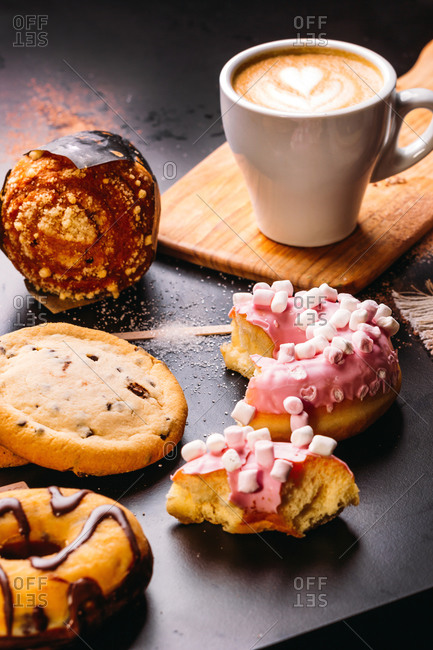 Various doughnuts with sweet toppings and chocolate bars composed with cup of cappuccino on black table