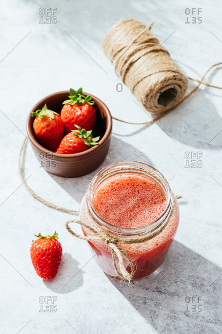 From above composition with fresh homemade strawberry juice in glass jar wrapped with twine placed on marble surface with whole berries
