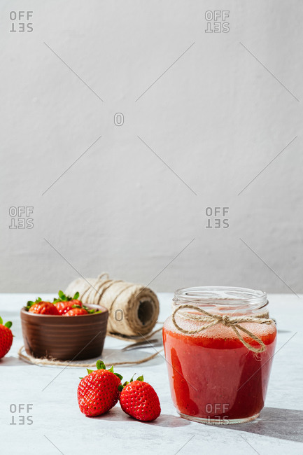 Composition with fresh homemade strawberry juice in glass jar wrapped with twine placed on marble surface with whole berries