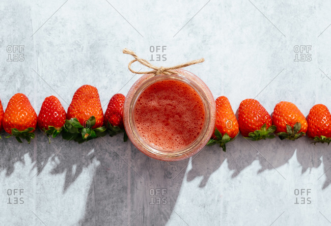 Composition with fresh homemade strawberry juice in glass jar wrapped with twine placed on marble surface with whole berries